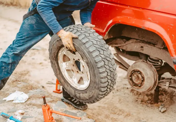 Persona con guanti smonta una gomma auto da un fuoristrada rosso. Si vede un cric arancione a terra, utile per capire dove smaltire gomme auto usate.