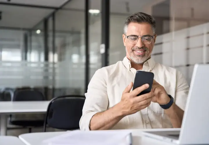 Uśmiechnięty mężczyzna z telefonem w dłoni, szukający informacji, jak udostępnić internet z telefonu na laptopa.