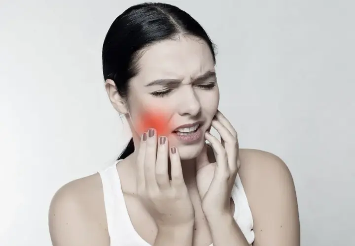 Mujer con dolor, tocándose la mejilla donde se ve un bulto mejilla interna enrojecido.