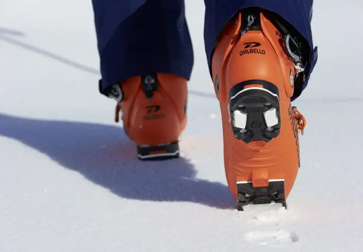 Botas de esquí naranjas Dalbello con suela de **grip walk** en la nieve, listas para la aventura.