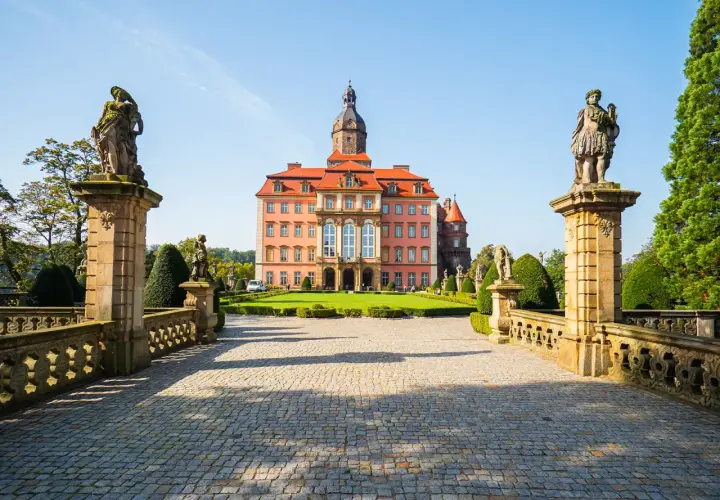 Zamek Książ z różową fasadą i wieżą, otoczony ogrodem. Poznaj zamek Książ ciekawostki i jego tajemnice.