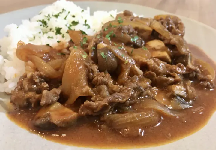 A plate of Hayashi Rice, featuring tender beef and onions in a rich demi-glace sauce served over fluffy white rice, garnished with parsley.