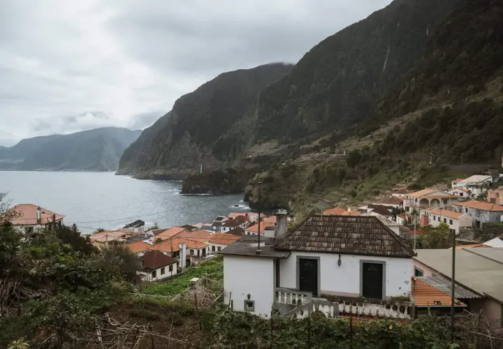 Coastal village with red-tiled roofs nestled against lush green mountains. A perfect place to stay in Madeira, offering stunning ocean views.