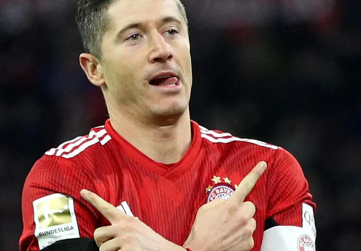Robert Lewandowski w czerwonej koszulce Bayernu z naszywką Bundesligi, wykonuje gest radości po strzelonej bramce.