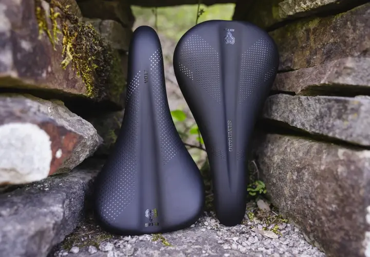 Two black WTB bike saddles, a Volt and a Silverado, rest against a stone wall, ready for adventure.