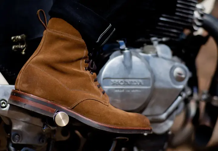 A suede boot rests on a motorcycle engine, ready for a ride. Learn how to walk in boots like these for style and comfort.