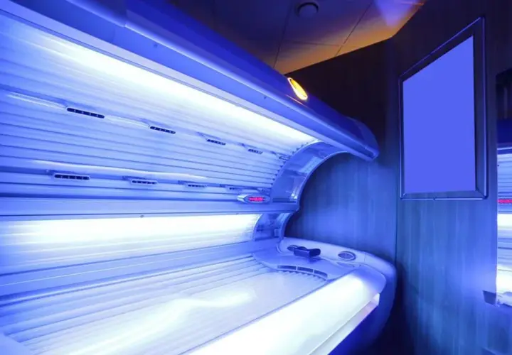 Wnętrze solarium z łóżkiem do opalania. Jasne lampy emitują niebieskie światło, tworząc atmosferę relaksu i przygotowania do letniego okresu.
