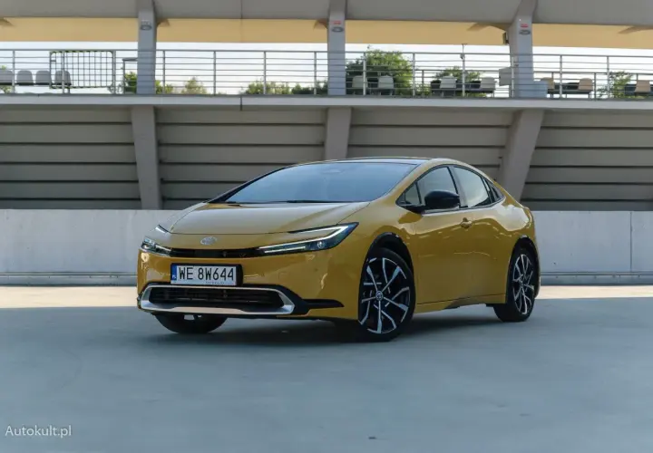 Nowy żółty Toyota Prius z nowoczesnym designem stoi na betonowym placu przed trybunami stadionu.