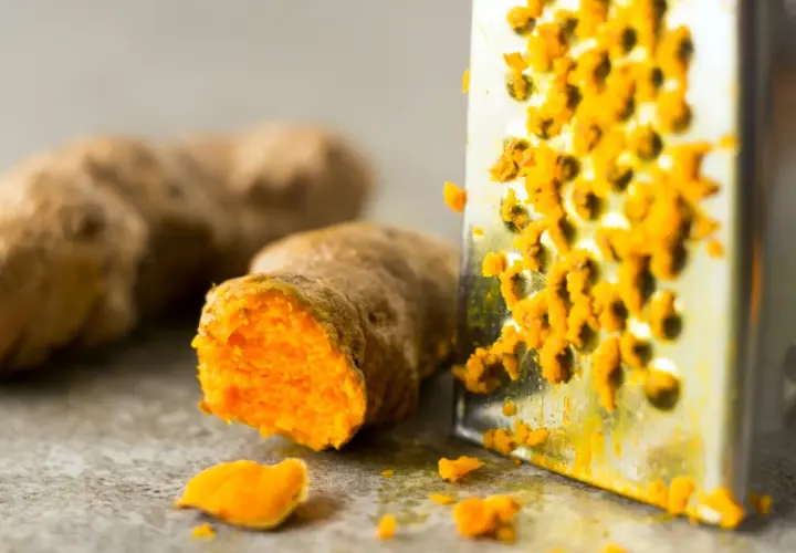 Frisch geriebene Kurkuma auf einem Metallreibe. So lässt sich die leuchtend orangefarbene Wurzel für die Lagerung vorbereiten.