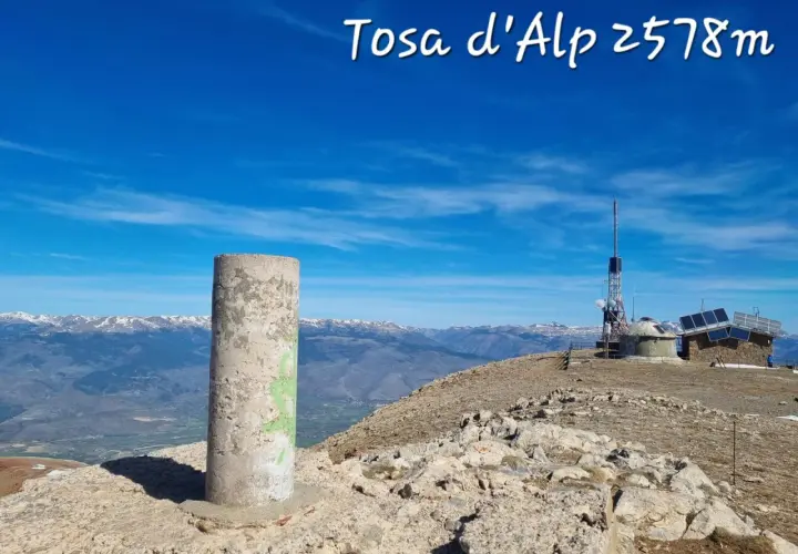 Cima de Tosa d'Alp, 2578m. Pilar de hormigón y antena de telecomunicaciones en un día soleado con vistas a montañas nevadas.