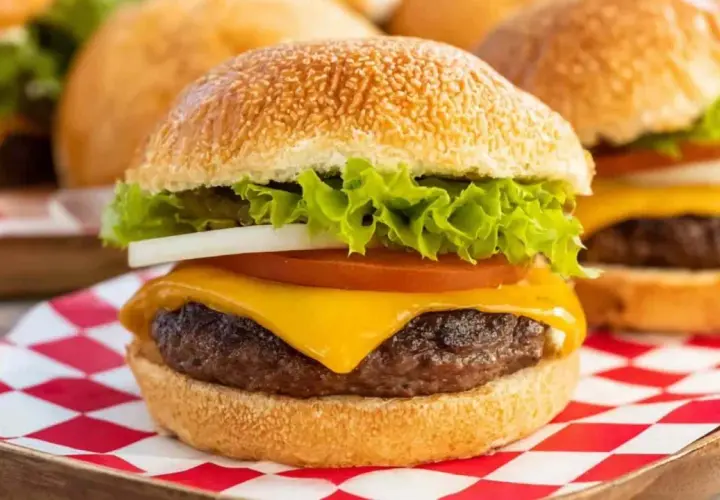 Soczyste mięso na burgery z serem, sałatą, pomidorem i cebulą, podane na kratkowanej serwetce.