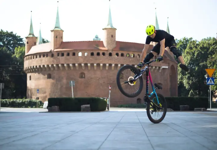 Rowerzysta wykonuje trik na tle Barbakanu. Odkryj **szlaki rowerowe Kraków** i poczuj wolność!