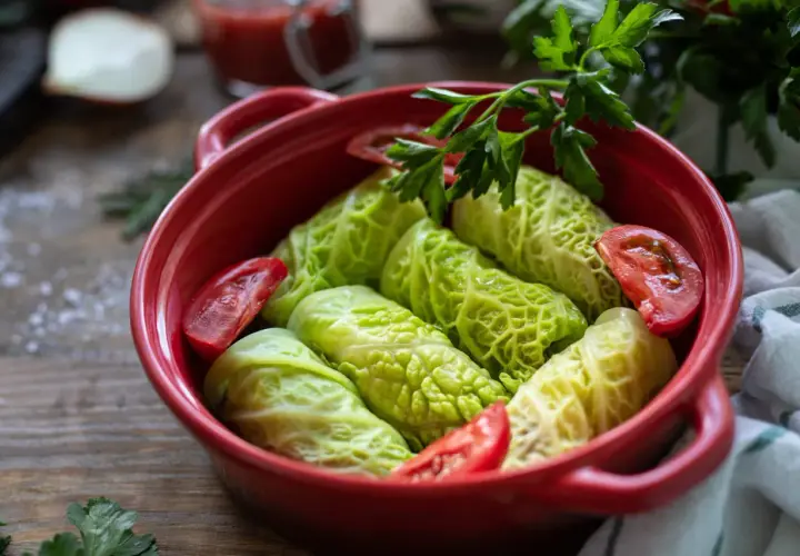 Choux verts au four prêts à cuire, garnissent un plat rouge avec des tomates et du persil frais.