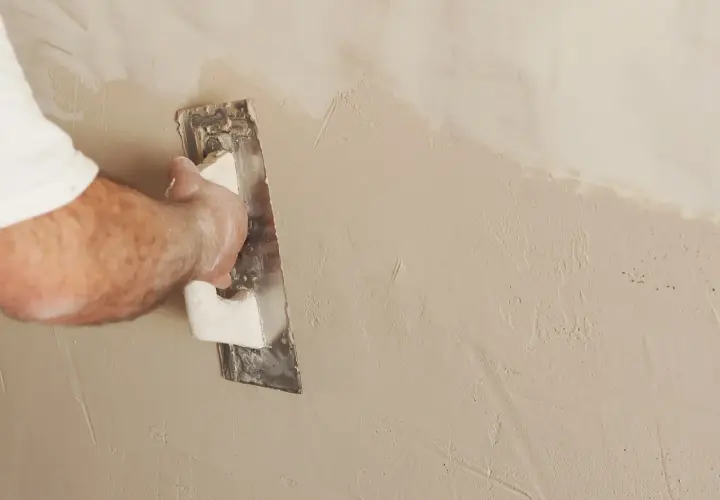 Mano che esegue la rasatura di un muro con una spatola, creando una finitura liscia e uniforme.