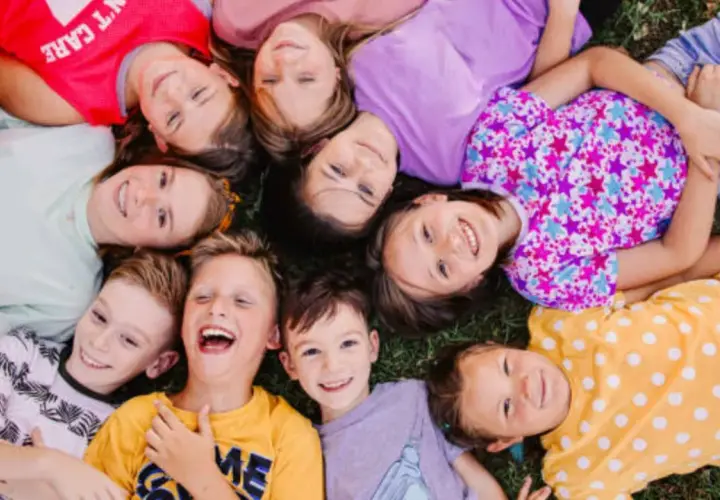 Niños sonriendo y jugando juntos en la hierba, una escena alegre de escuela de verano para niños de 2 años.