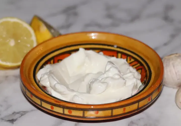 Krämig vitlökssås, perfekt för ditt toum recept. Citron och vitlök bredvid skålen.