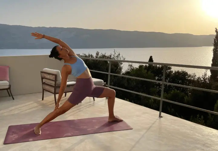 Mujer en postura de yoga en terraza con vista al mar al atardecer. Un momento de **slow life** y conexión.