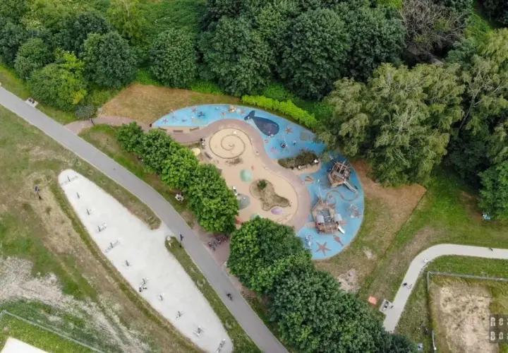 Kolorowy plac zabaw w kształcie fali z wielorybem i statkami pirackimi, otoczony zielenią. Idealne miejsce na zabawę dla dzieci w Łodzi.