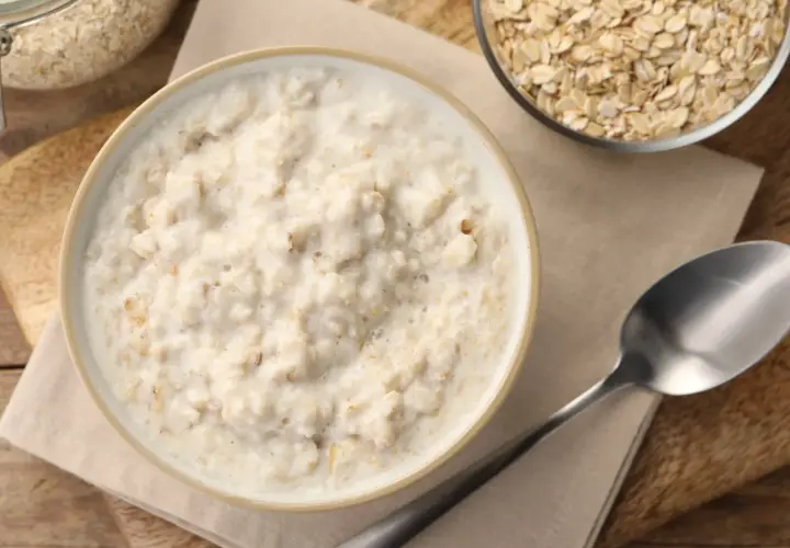 Miseczka kremowego congee z płatków owsianych, obok słoik i miseczka z płatkami. Idealne na śniadanie.