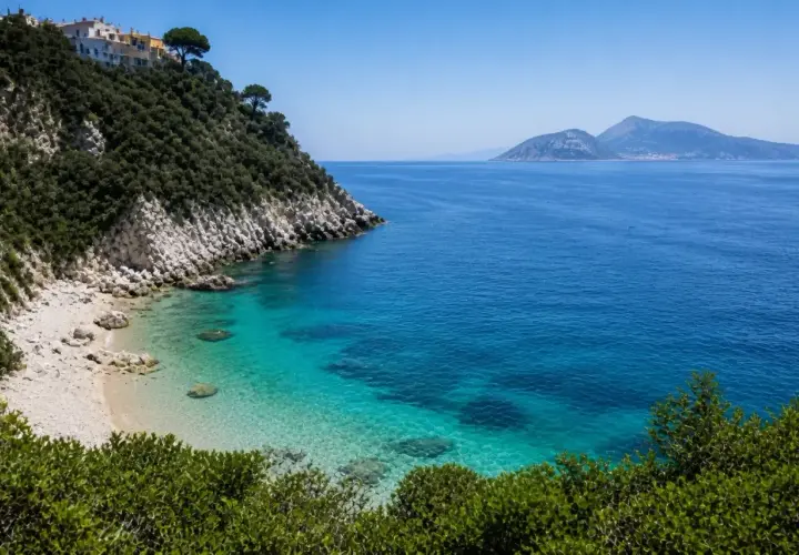 Vue d'une crique aux eaux turquoise cristallines, avec une colline verdoyante et des maisons blanches perchées, près d'une île à côté de Capri.