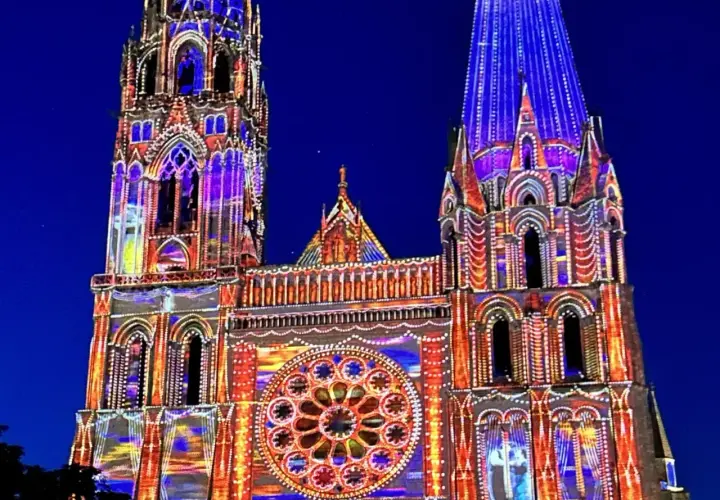 Katedra w Chartres nocą, rozświetlona kolorowymi projekcjami. Architektura gotycka w odcieniach niebieskiego i pomarańczowego.