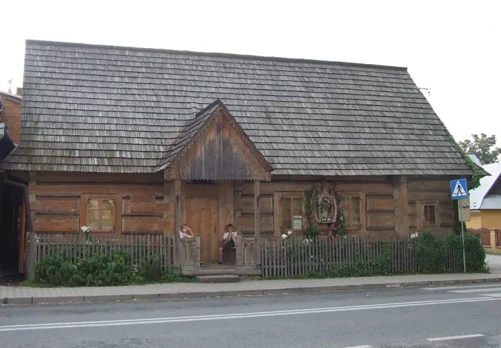 Drewniany budynek muzeum powstania chochołowskiego z gontowym dachem. Dzieci siedzą na progu.