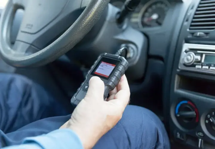 Ręka trzymająca skaner diagnostyczny OBD w samochodzie.