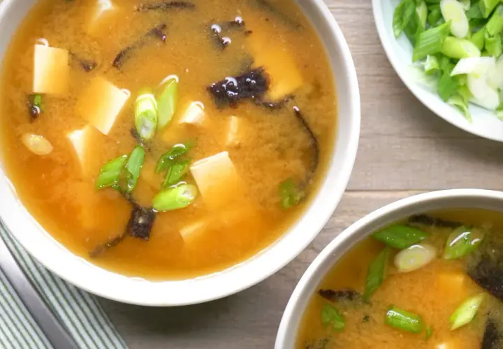 Two bowls of steaming nori soup, filled with tofu cubes and green onions, are ready to be enjoyed.