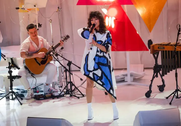 Wokalistka w sukience z geometrycznym wzorem śpiewa na scenie podczas MTV Unplugged Polska. Obok gra gitarzysta.