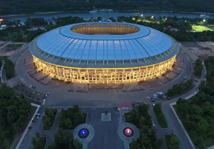 Oświetlony moskiewski stadion w nocy, z widokiem na rzekę i otaczający go las.