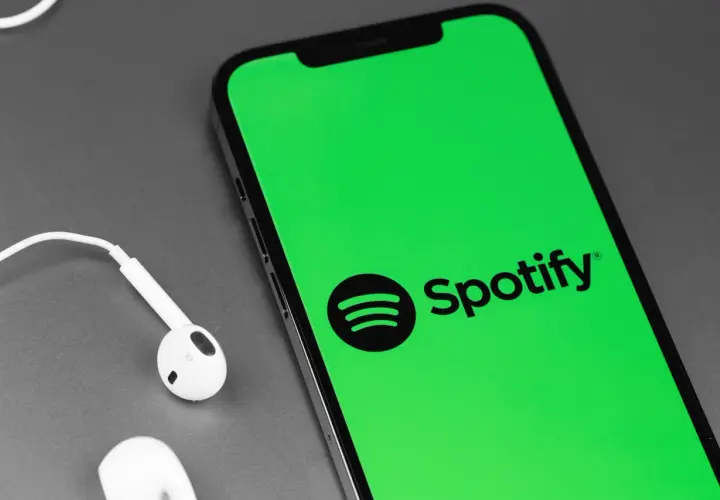 Telefon z zielonym ekranem i logo Spotify, obok białe słuchawki. Słuchaj muzyki za darmo dzięki Spotify free.