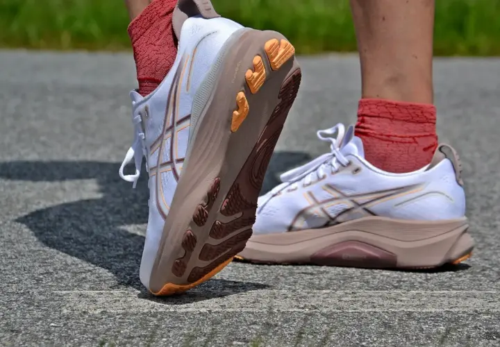 Białe buty do biegania Asics z pomarańczowymi akcentami na podeszwie. Firma Asics słynie z innowacyjnych rozwiązań.