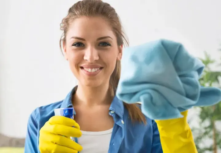 Donna sorridente con guanti gialli e panno blu, pronta a pulire le vetrate scorrevoli.