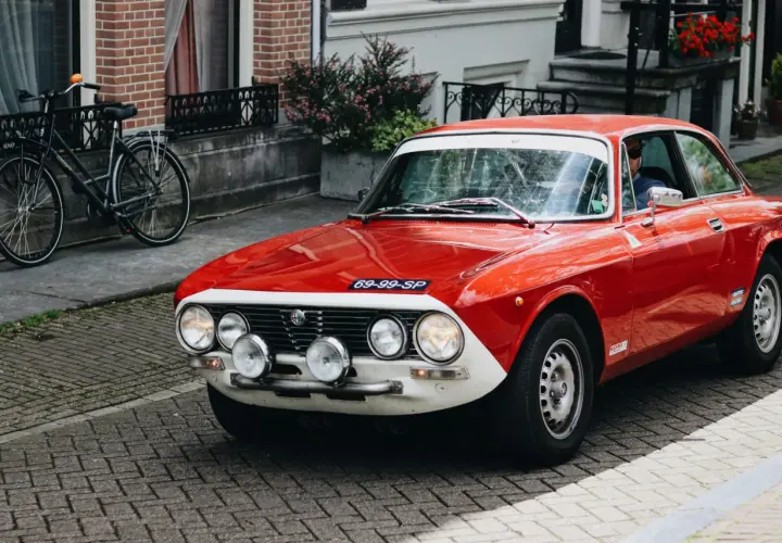 Czerwone auto sportowe Alfa Romeo z lat 70. na brukowanej ulicy, obok rower.