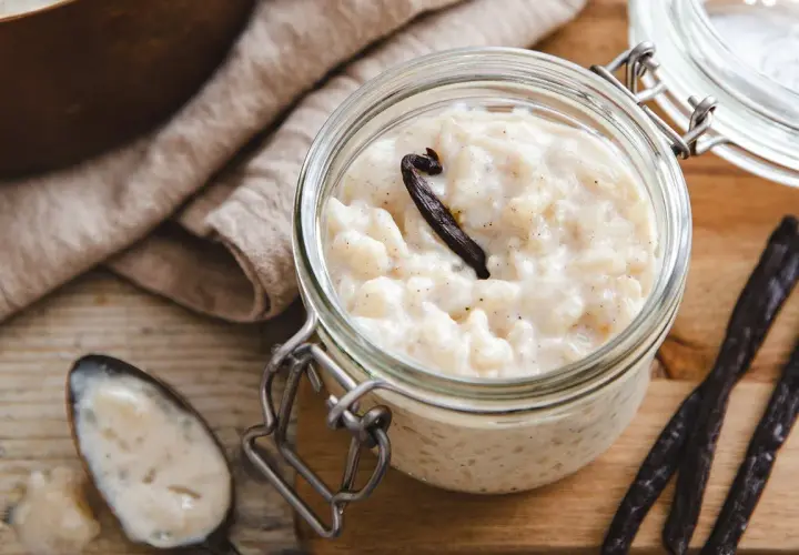 Un pot en verre rempli de riz au lait au four, garni d'une gousse de vanille. Une cuillère à côté en témoigne.