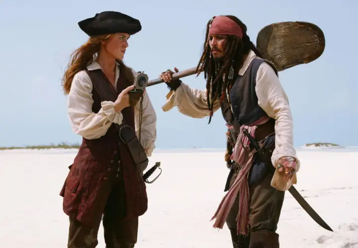 Elizabeth Swann i Kapitan Jack Sparrow, bohaterowie filmów "Piraci z Karaibów", stoją na plaży, rozmawiając.