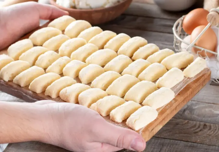 Gotowe do gotowania kluski leniwe, przepis babci. Na desce ułożone rzędy pierożków z twarogu, obok jajka i twaróg.