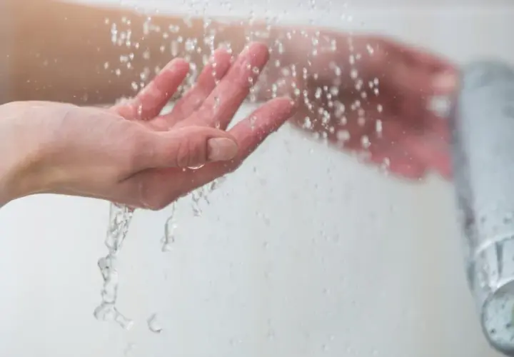Manos bajo un chorro de agua fría, sintiendo el frescor al ducharse con agua fría.