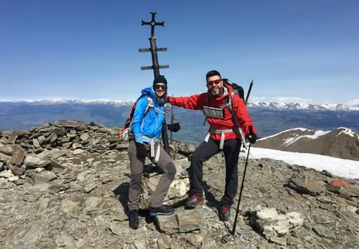 Dos montañistas celebran en la cima del Fontalba Puigmal, con un cruce metálico y vistas nevadas.