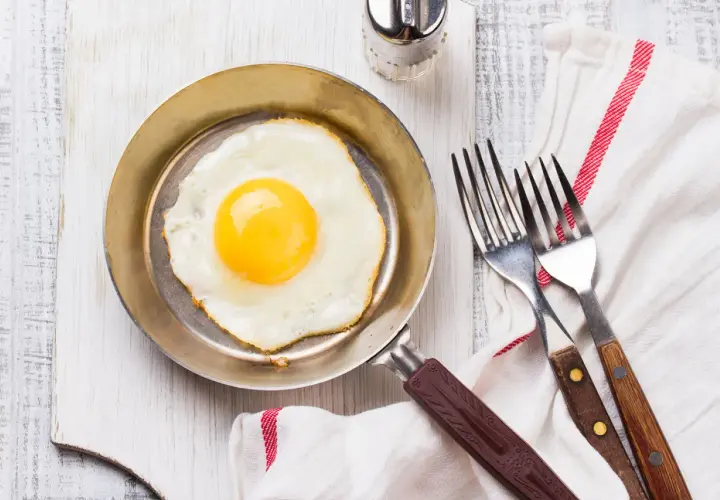 Un œuf au plat parfait, cuisiné dans une poêle inox, prêt à être dégusté avec deux fourchettes.