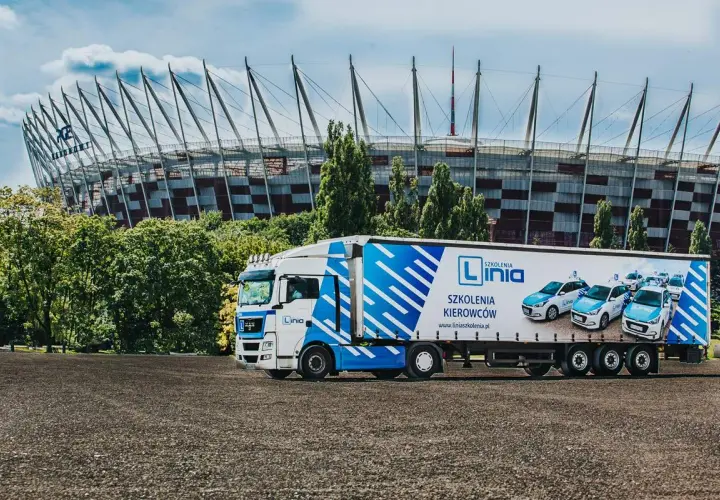 Ciężarówka z logo "Linia Szkolenia Kierowców" i samochodami na naczepie, na tle Stadionu Narodowego. Marzysz o **prawie jazdy na tira**? Tu możesz je zdobyć!