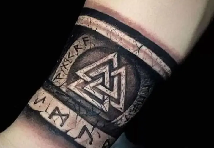 Tatuaż na przedramieniu z nordyckimi symbolami: Valhalla i runy. Wygląda jak starożytny artefakt.