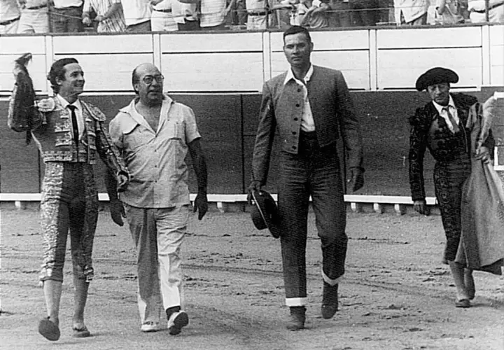 Un sayalero y un bandrés caminan juntos en la arena. El sayalero, con traje de luces, saluda.