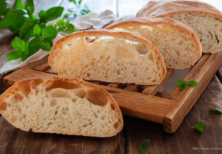 Fette di pane soffice con alveolatura pronunciata, su un tagliere di legno, con foglie di menta fresca.