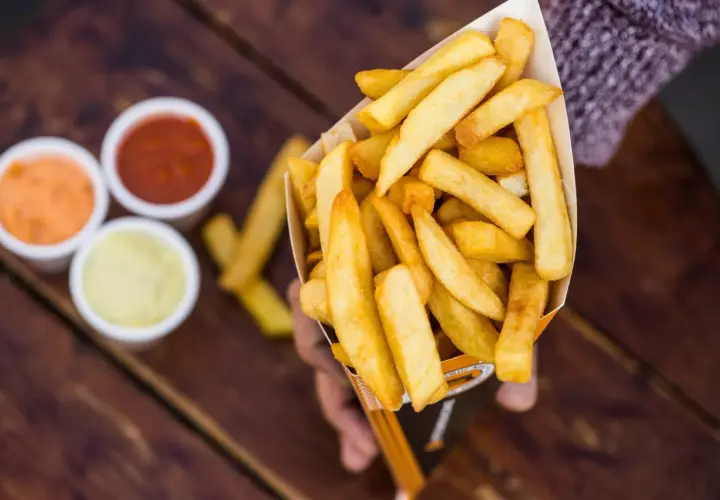 Idealny dzień frytek! Złociste frytki w papierowym rożku, obok trzy sosy: ketchup, majonez i sos czosnkowy.