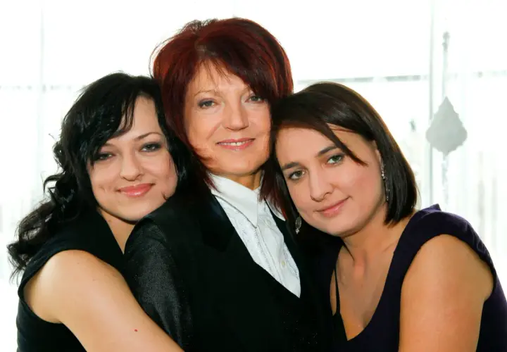 Trzy kobiety: starsza z rudymi włosami w czarnej marynarce i dwie młodsze, córki, obejmujące ją.