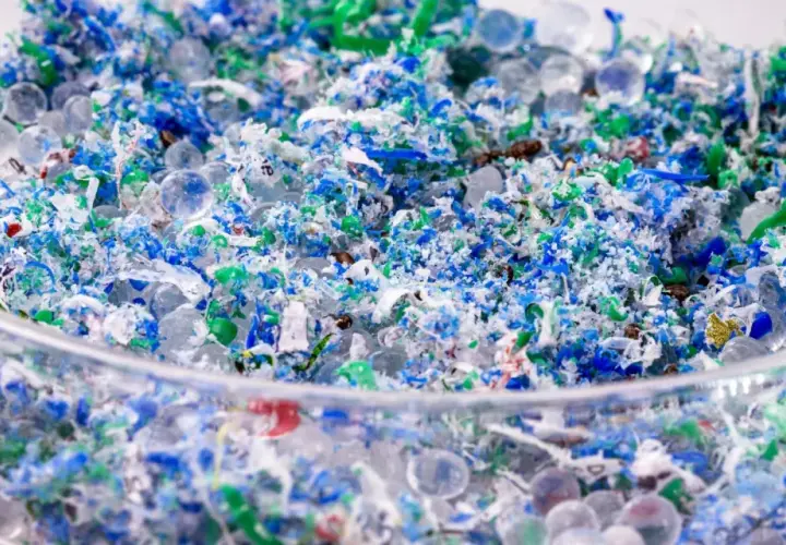 Kolorowe fragmenty plastiku i przezroczyste kuleczki, przypominające mikrokoraliki, tworzą obraz zanieczyszczenia. To mikroplastik w wodzie, widoczny w szklanym naczyniu.
