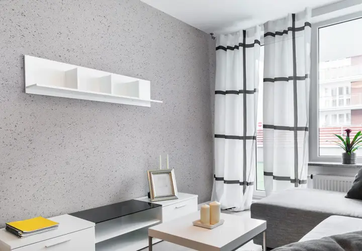 Nowoczesny salon z szarą ścianą pokrytą tynkiem japońskim o subtelnych wzorach. Białe meble i zasłony w kratę.