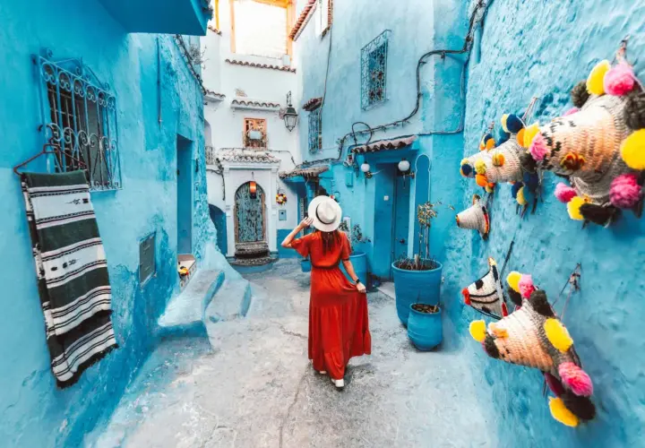 Una mujer con vestido rojo pasea por una calle de la **marruecos ciudad azul**, decorada con coloridas artesanías.