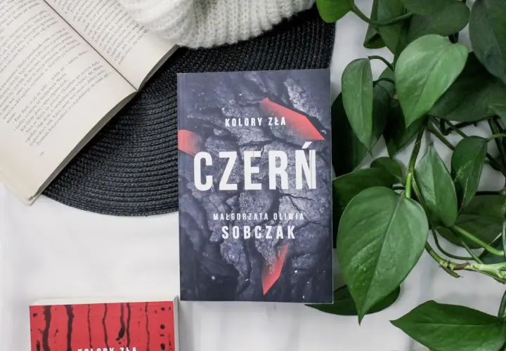 Kolory zła: Czerń. Filmowa okładka książki Małgorzaty Olwii Sobczak, otoczona zielonymi liśćmi i innymi książkami.